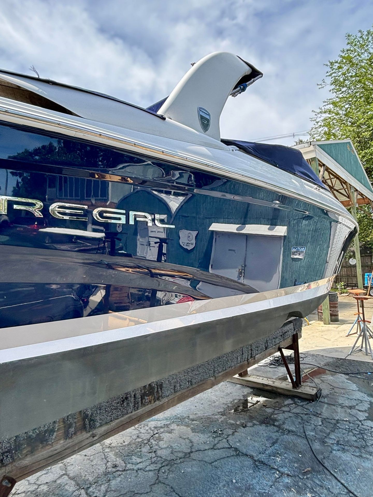 Close-up of a yacht's exterior on a stand, with visible reflections and overcast sky.